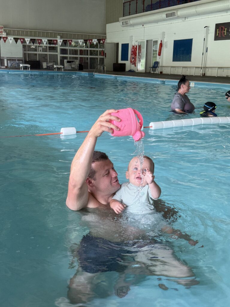 Dad gently pouring water over his baby during a swimming class