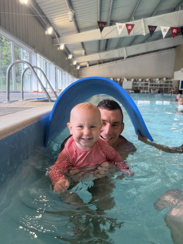 Smiling baby swimming through a float arch with her dad